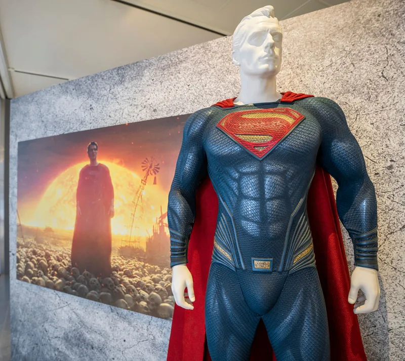 Traje de Superman sobre un maniquí frente al panel con el marco de Superman en negro al atardecer.