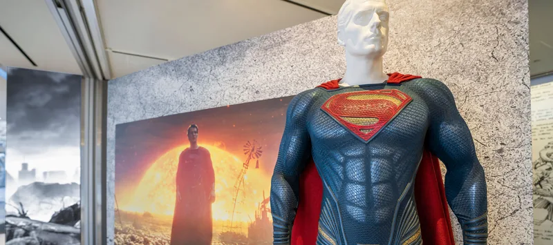Disfraz de Superman de cuerpo entero frente al panel de Superman al atardecer