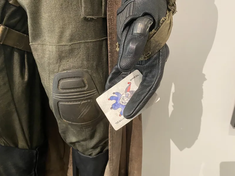 Primer plano del guante y la rodillera del disfraz de Knightmare Batman, con la etiqueta de colección colgando